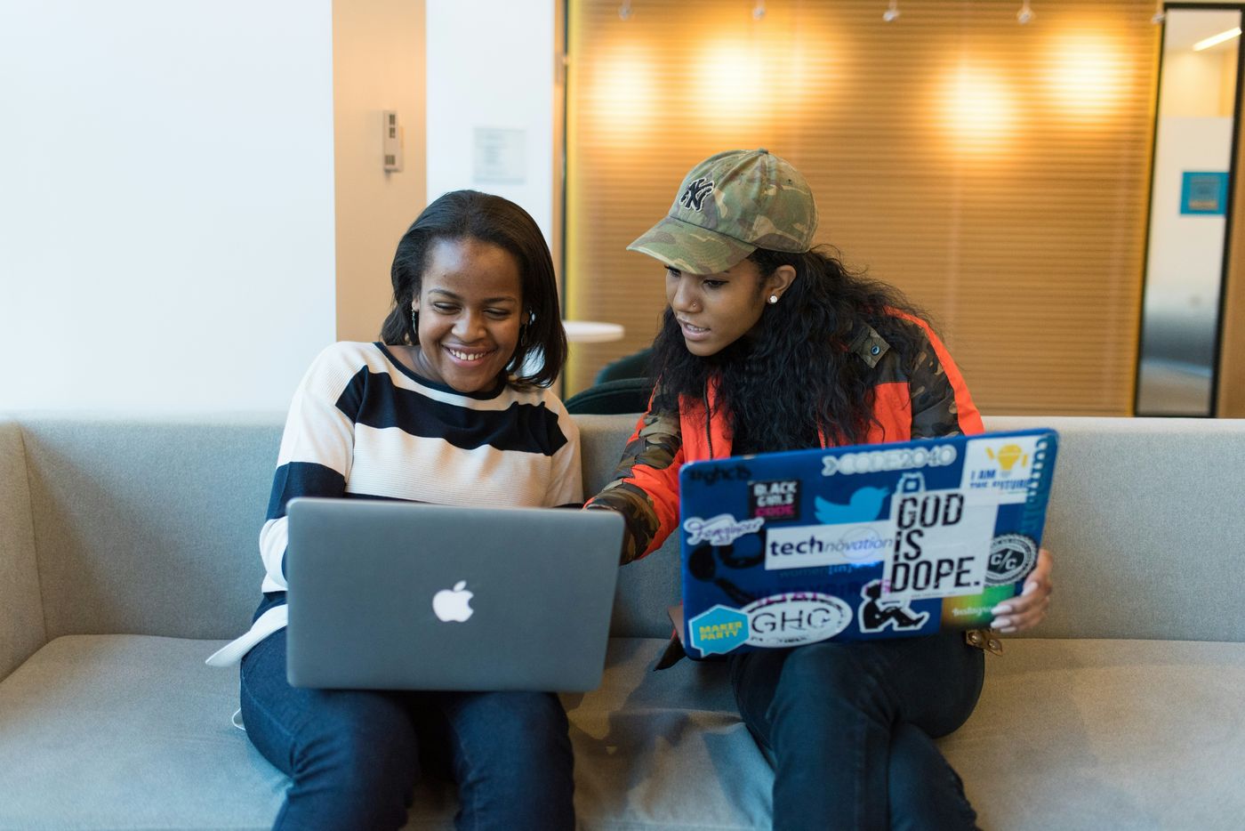 Dos mujeres ríen mientras trabajan con sus laptops llenas de stickers
